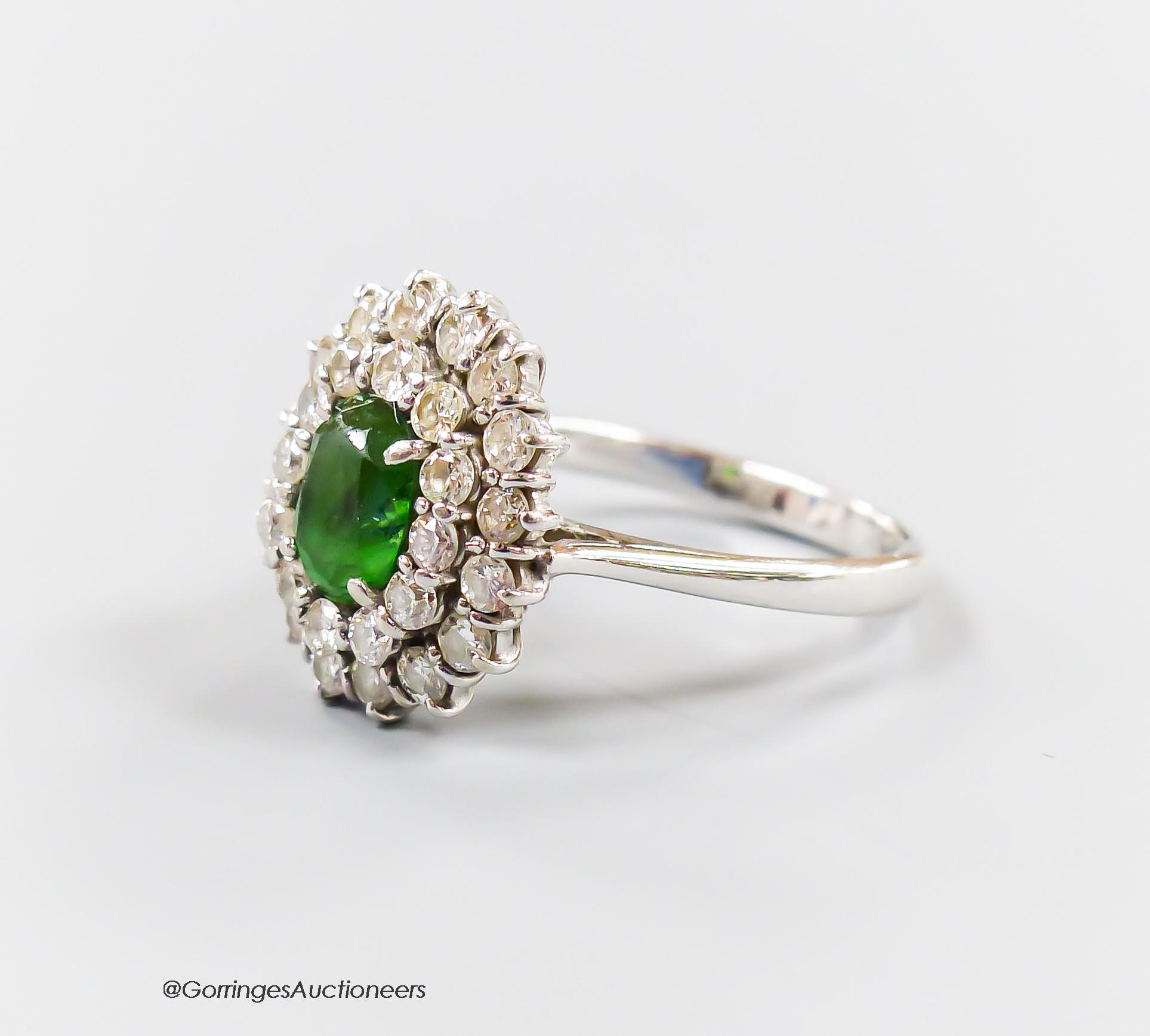 A modern 18ct white gold, green garnet and diamond set oval cluster ring, size N, gross weight 5.3 grams.